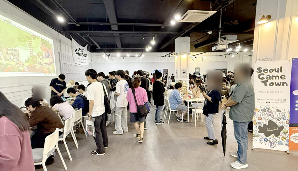 제1회 서울게임타운: 게임 시연 테이블과 안내 배너 사이를 둘러보는 관람객