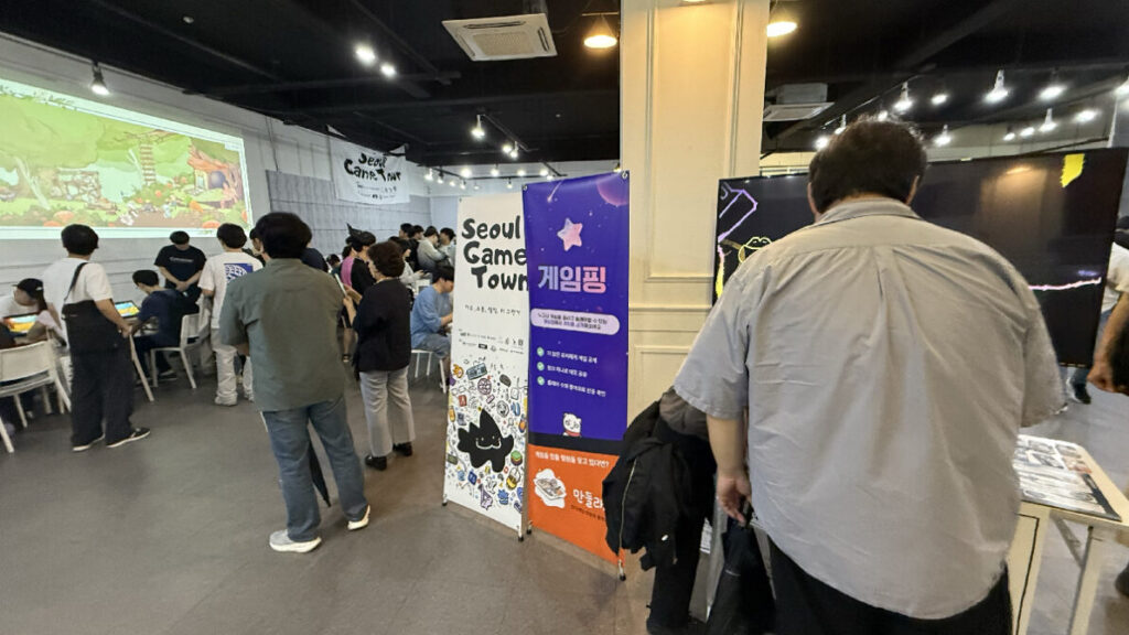 제1회 서울게임타운: 게임 화면을 비춘 벽면 앞에서 전시를 관람하는 사람들