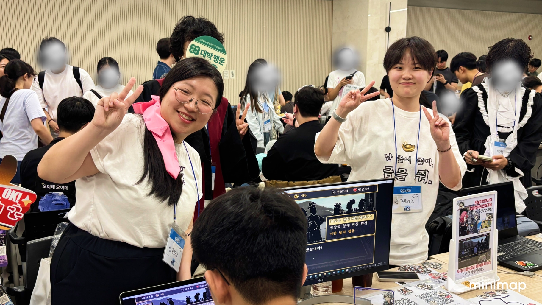 제2회 서울게임타운: 모니터가 놓인 전시 부스에서 손으로 브이 포즈를 하는 두 참가자